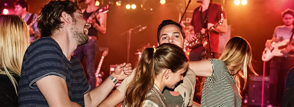 Eine Gruppe tanzt ausgelassen. Im Hintergrund spielt eine Band.