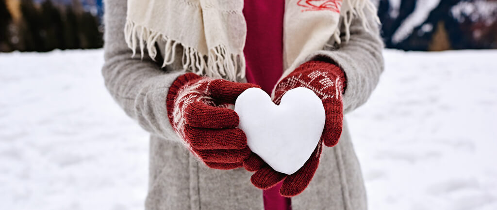 Eine Person mit Handschuhen hält ein aus Schnee geformtes Herz in de Händen.